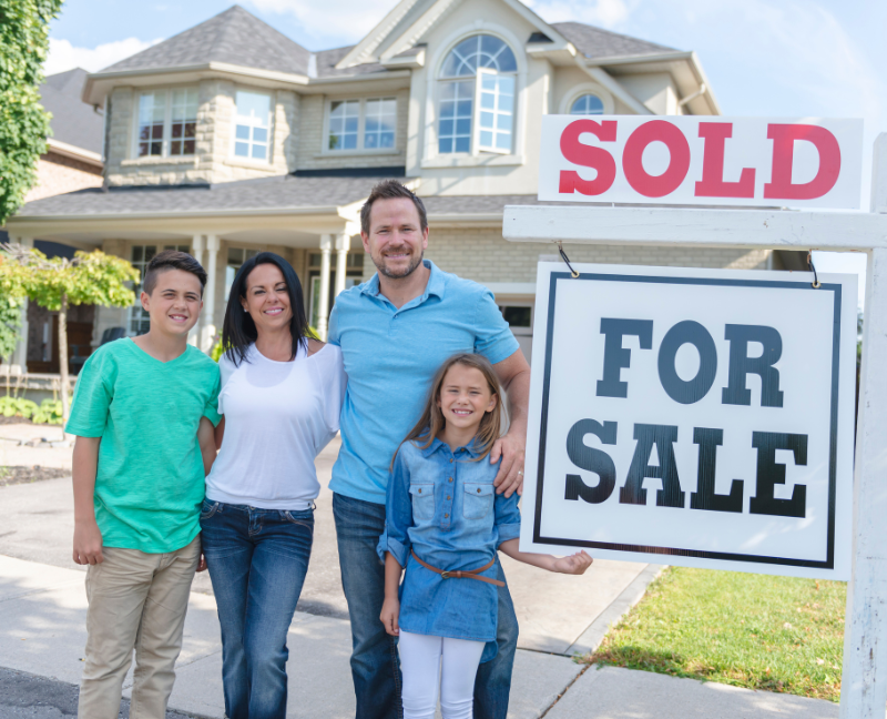 family posing in front of new house with sold for sale sign