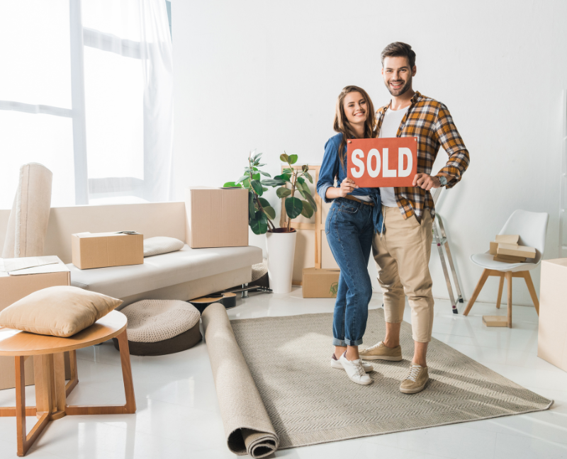 couple holding sold sign in new home