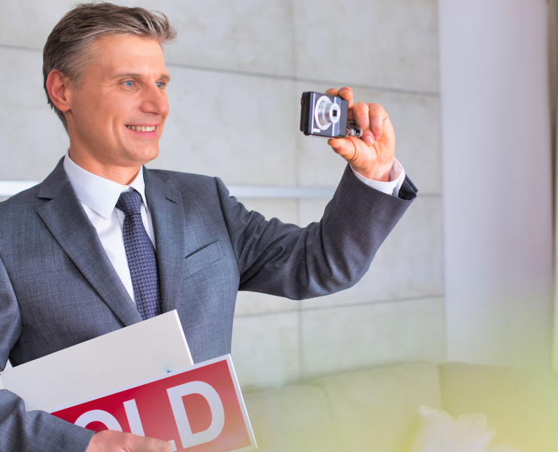 real estate agent taking photo while holding sold sign
